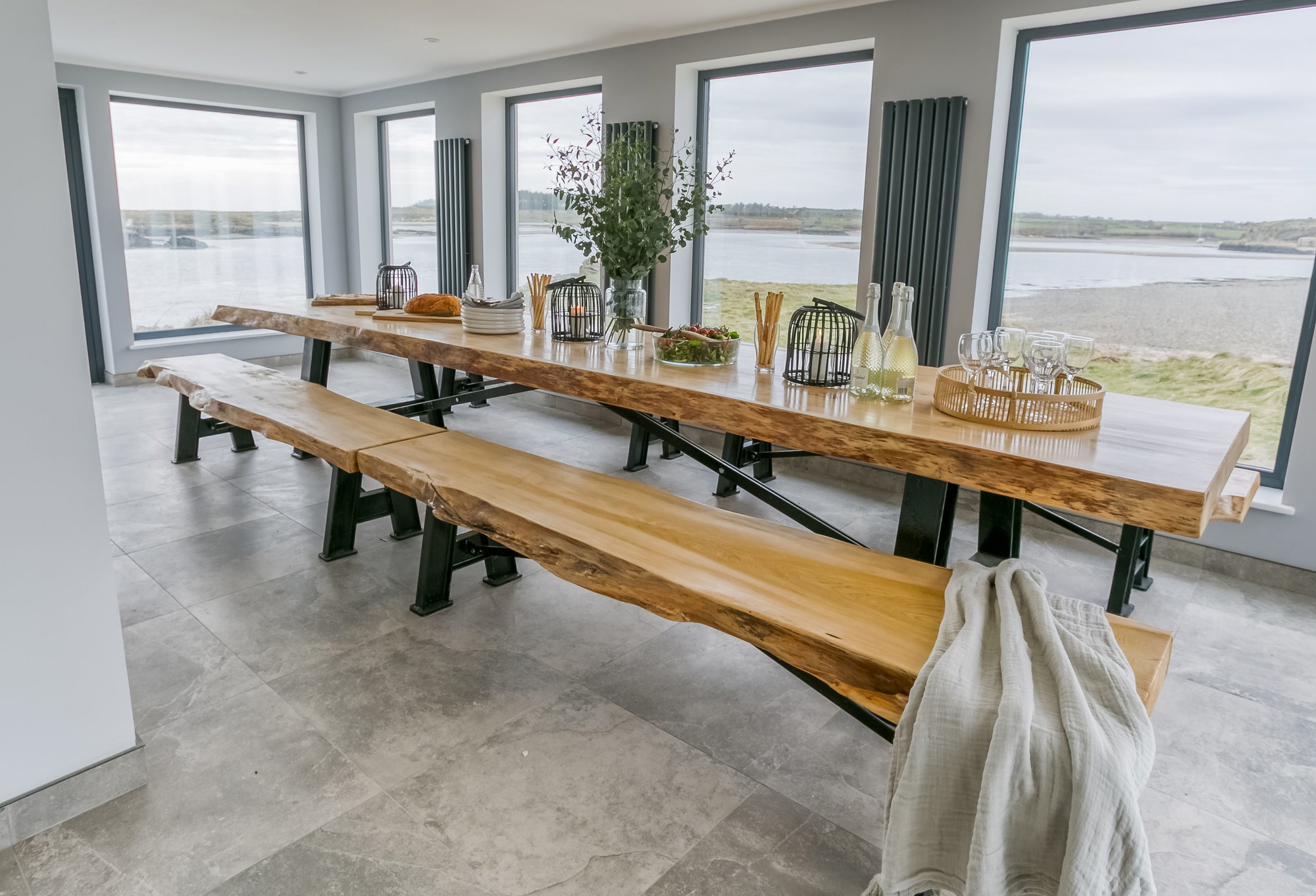 The long cedar dining table seating sixteen in front of full-height windows onto the sea